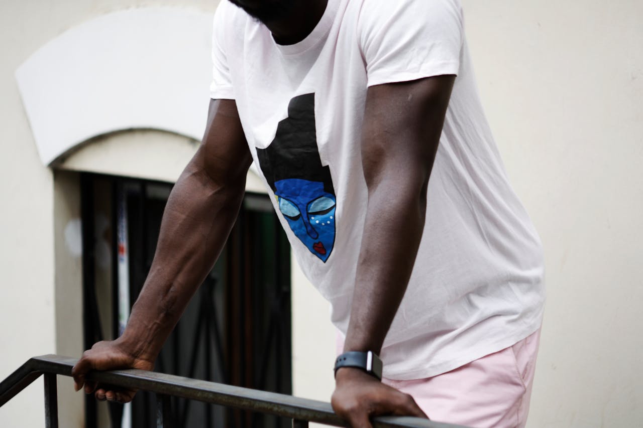 services-02 Man wearing a white t-shirt with a colorful artistic design, leaning on a handrail.