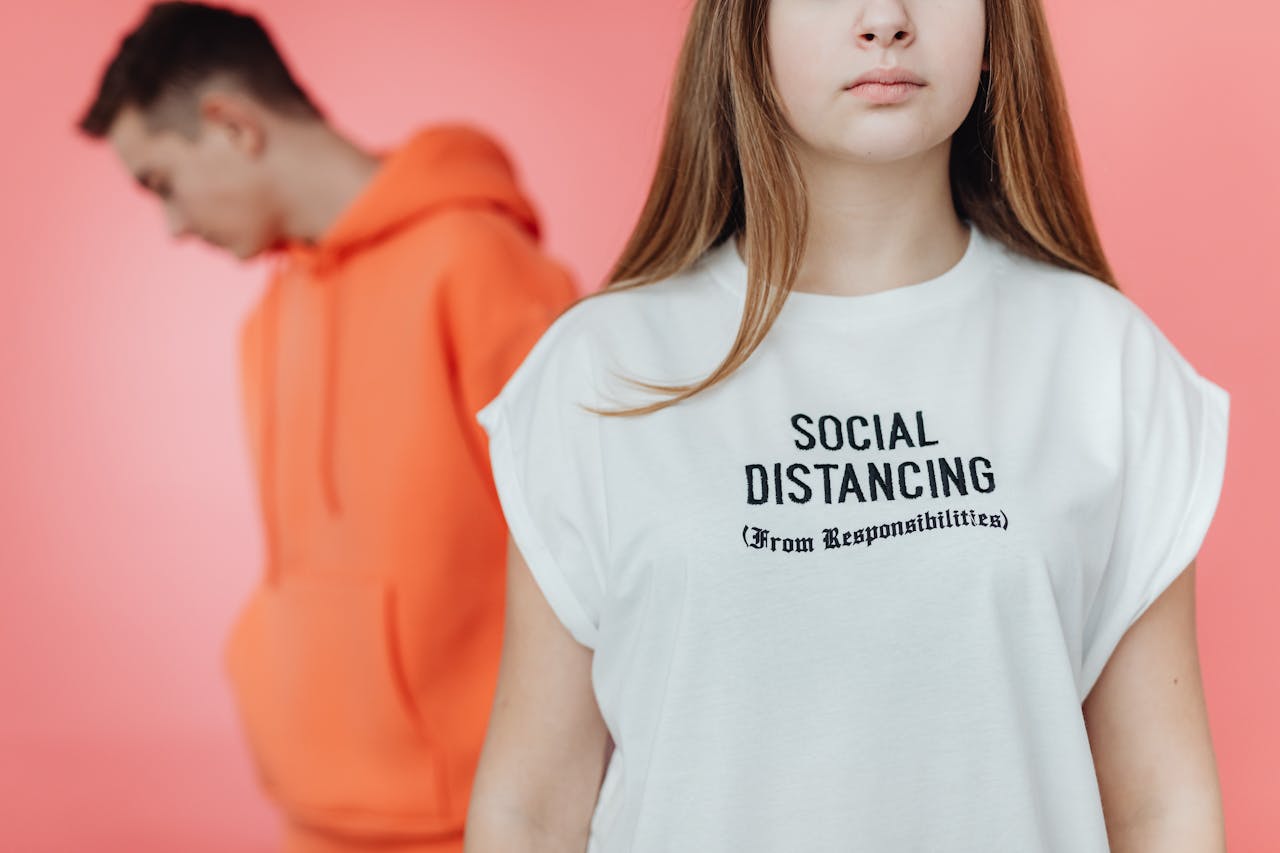 services-01 Young adults wearing trendy hoodies with a humorous social distancing message on a blurred background.